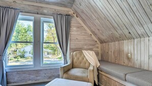 Une pièce chaleureuse avec un plafond en bois, un banc rembourré, un fauteuil confortable et une grande fenêtre avec des rideaux.