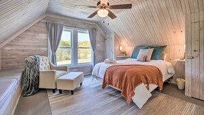 Une chambre mansardée chaleureuse avec un plafond en pente, un grand lit recouvert d’une couverture marron, une chaise et un banc.