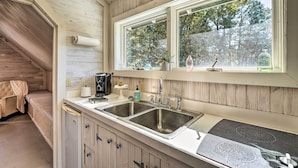 Une cuisine équipée d’un évier à deux bacs, de meubles en bois, d’une fenêtre donnant sur les arbres et d’un coin salon confortable avec un banc.