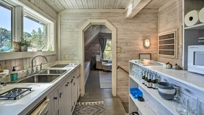 Une cuisine étroite aux murs en bois, dotée d’un îlot central et offrant une vue sur l’espace de vie.