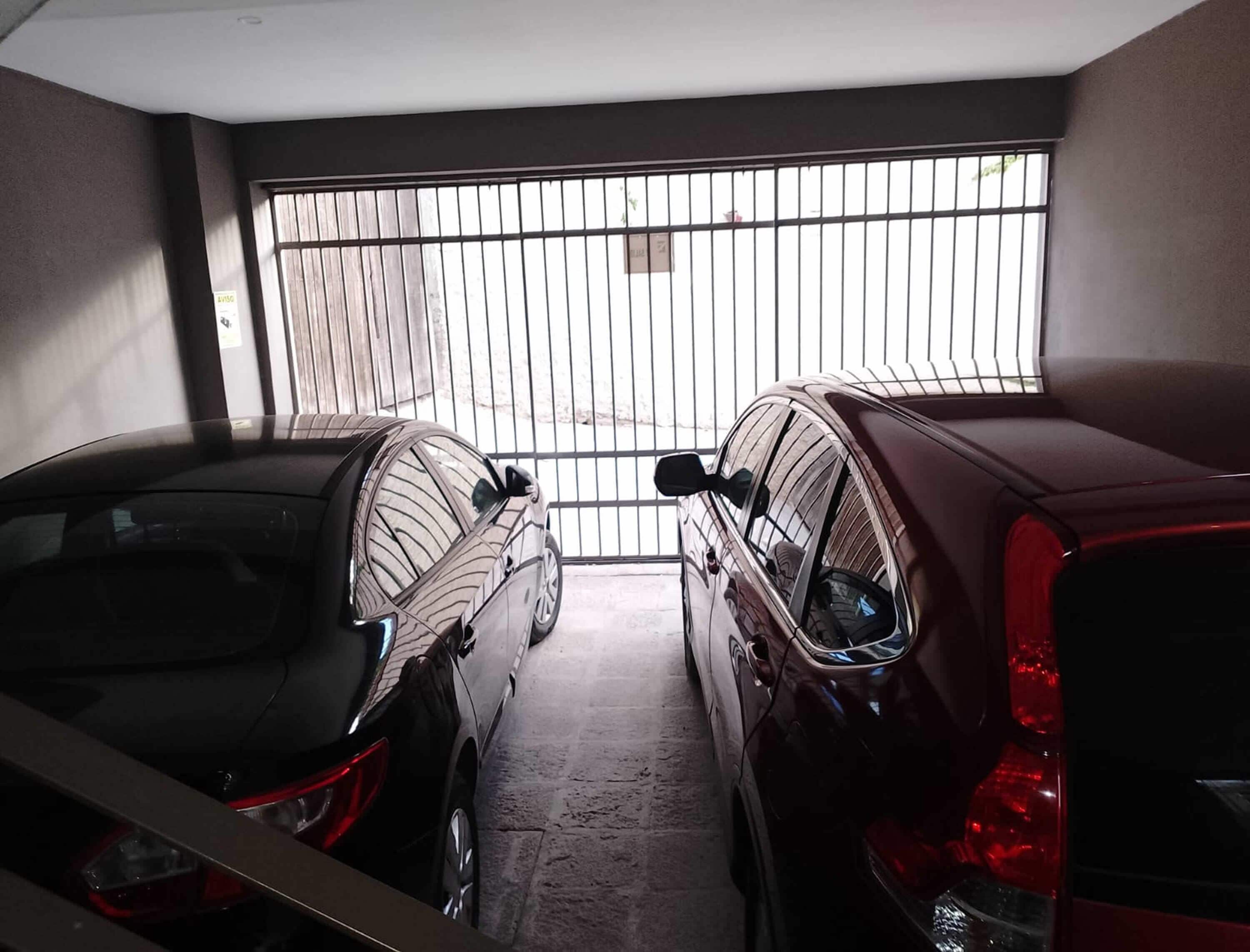 Un parking avec deux voitures garées côte à côte, une barrière métallique et un sol en béton.