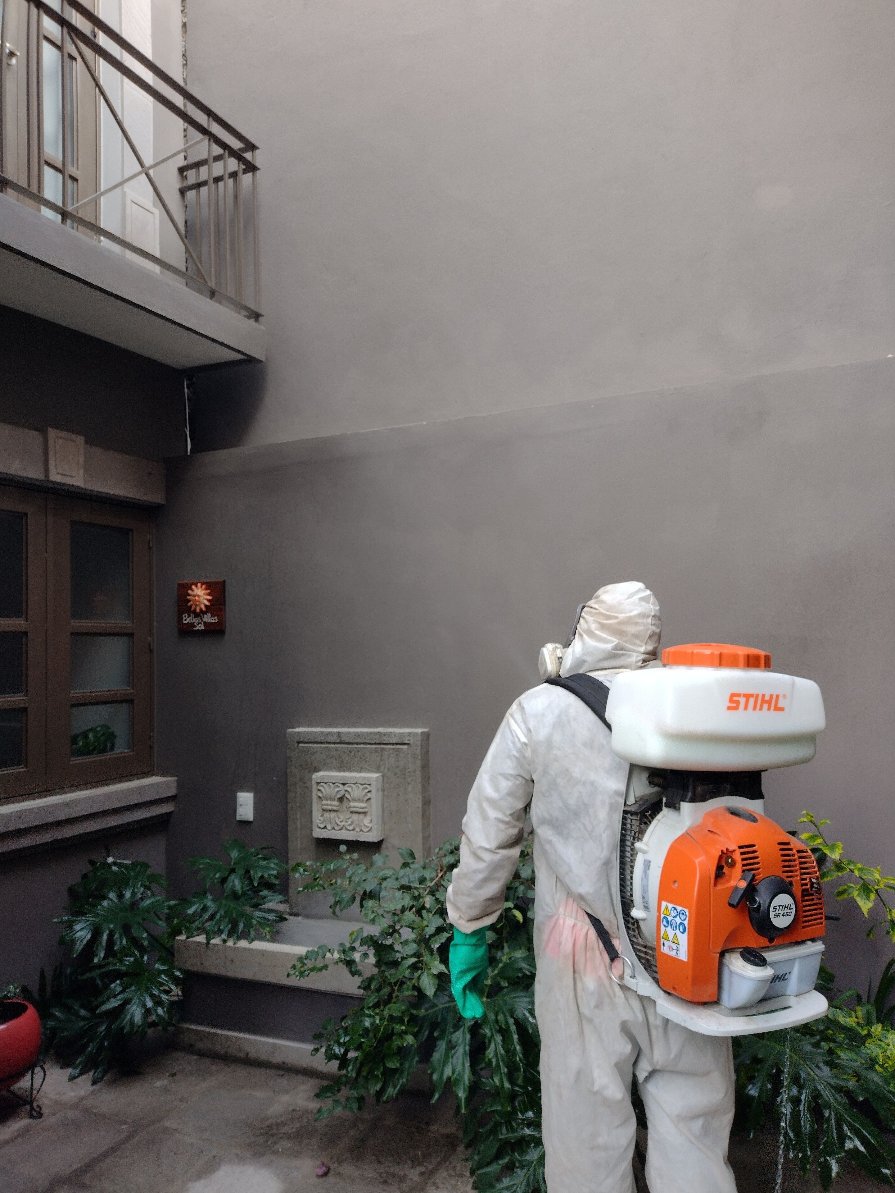 A person in protective gear spraying a wall with a pressure washer.