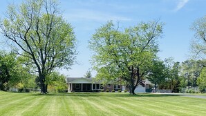 Une propriété résidentielle dotée d’une pelouse bien entretenue, d’une maison avec un porche et de grands arbres.