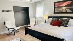 Een slaapkamer met een bed, een stoel, een bankje, een kledingkast en een schilderij aan de muur.