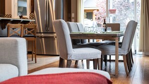 A modern kitchen with a stainless steel refrigerator, wooden cabinets, and a dining area with a wooden table and grey upholstered chairs. - Aspen Lodge by Revelstoke Vacations (Revelstoke)