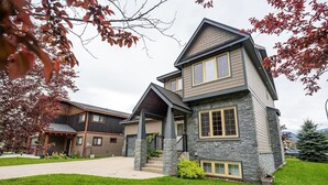 A two-story house with a stone facade, a front porch, and a well-maintained lawn. - Aspen Lodge by Revelstoke Vacations (Revelstoke)