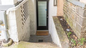 A narrow entrance with a black door, a welcome mat, and a metal grate.