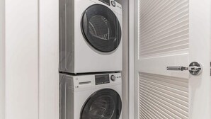 A laundry room with two stacked washing machines and a door with horizontal blinds.