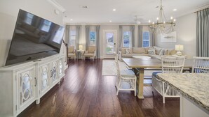 A spacious living room with a large flat-screen TV, a dining area with a marble table, and a cozy seating area with a sofa and chairs. - Steps to 30A - Golf Cart - Kid & Friendly! (Santa Rosa Beach)