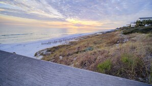 A beach with a wooden walkway, a fence, and a building with a sloped roof. - Steps to 30A - Golf Cart - Kid & Friendly! (Santa Rosa Beach)