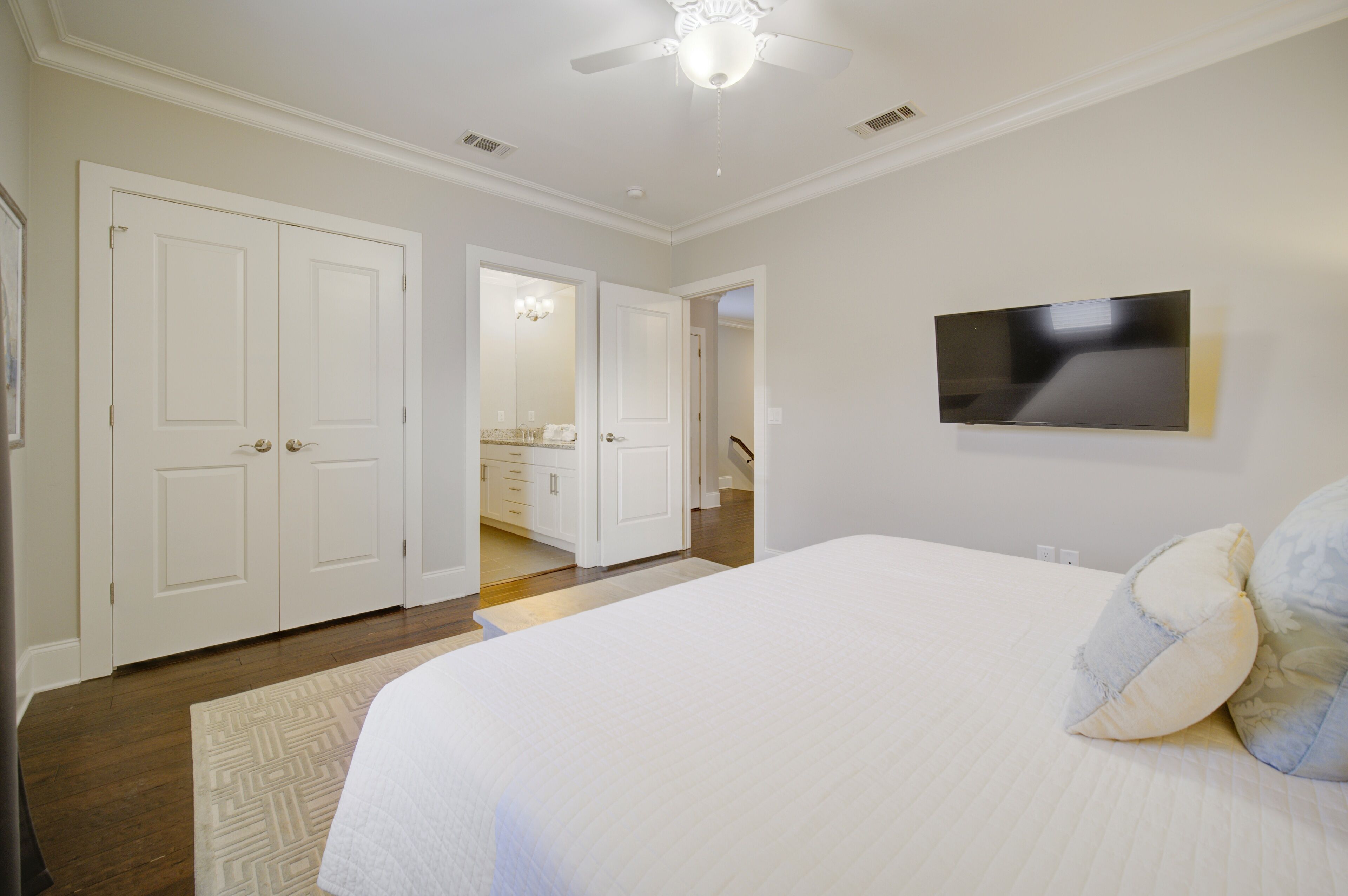 A bedroom with a large bed, a flat-screen TV mounted on the wall, and a ceiling fan.