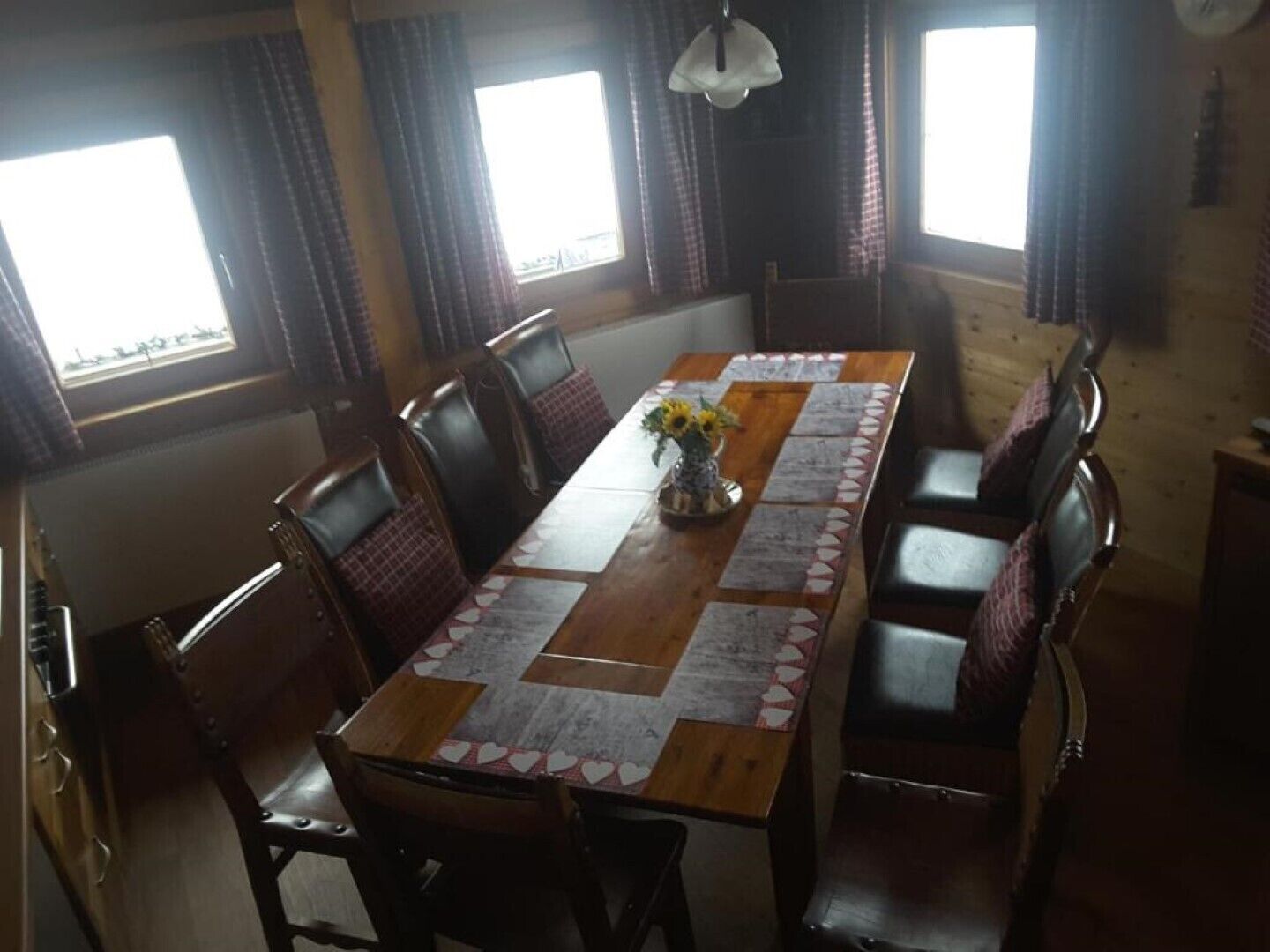A dining area with a long wooden table, multiple chairs, and a vase with sunflowers.