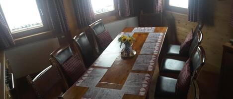 A dining area with a long wooden table, multiple chairs, and a vase with sunflowers.