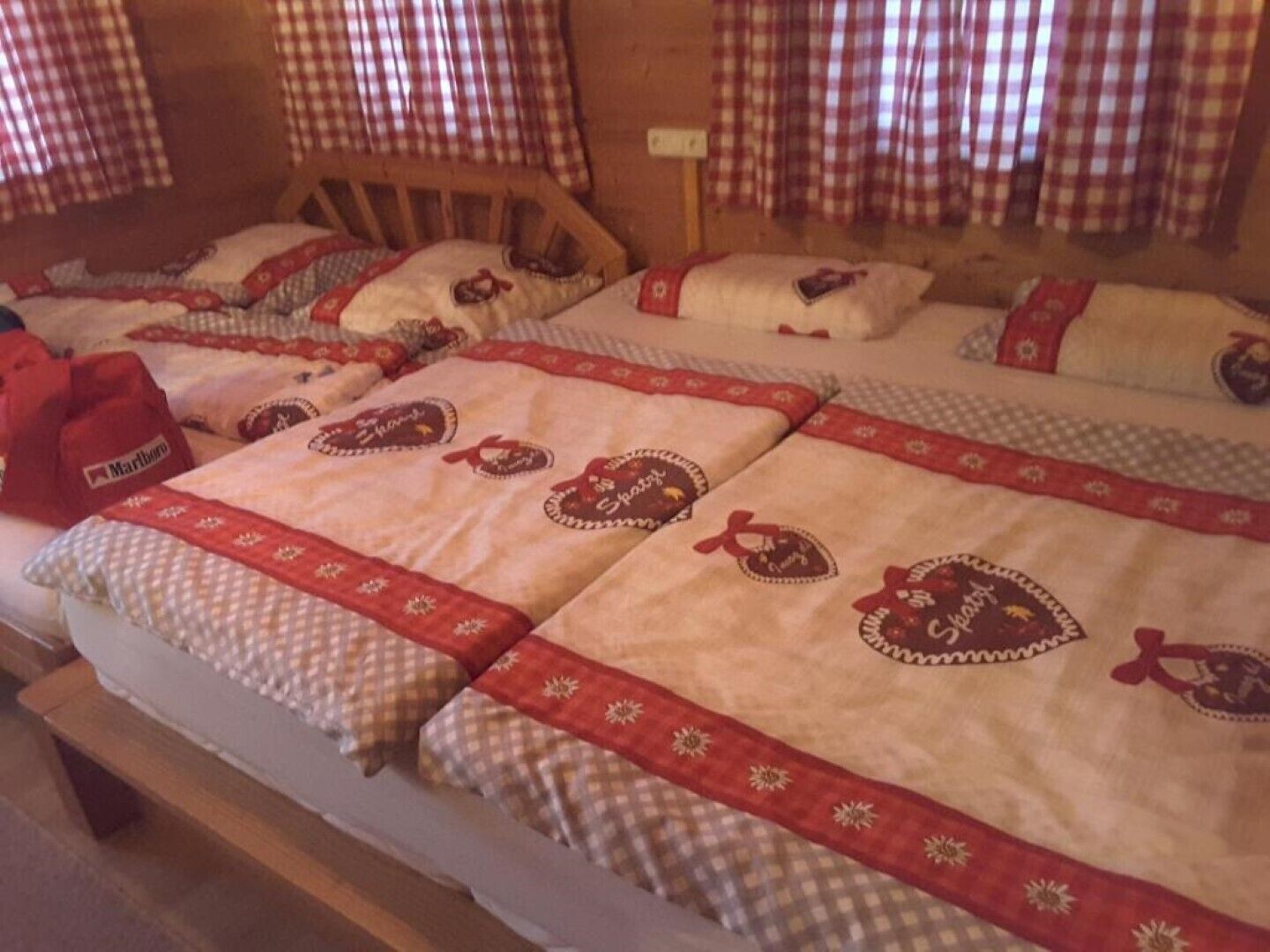 A room with multiple beds, each with a checkered blanket and a red border.