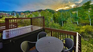 En terrasse med et bord og stole med udsigt over et bjergrigt landskab og bygninger i det fjerne.