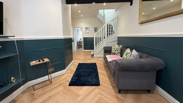 Un salon moderne avec un canapé gris, un tapis foncé et un escalier menant à l’étage supérieur.