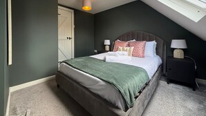 Une chambre avec un plafond en pente, un lit recouvert d’une couverture verte, deux lampes de chevet et une fenêtre.