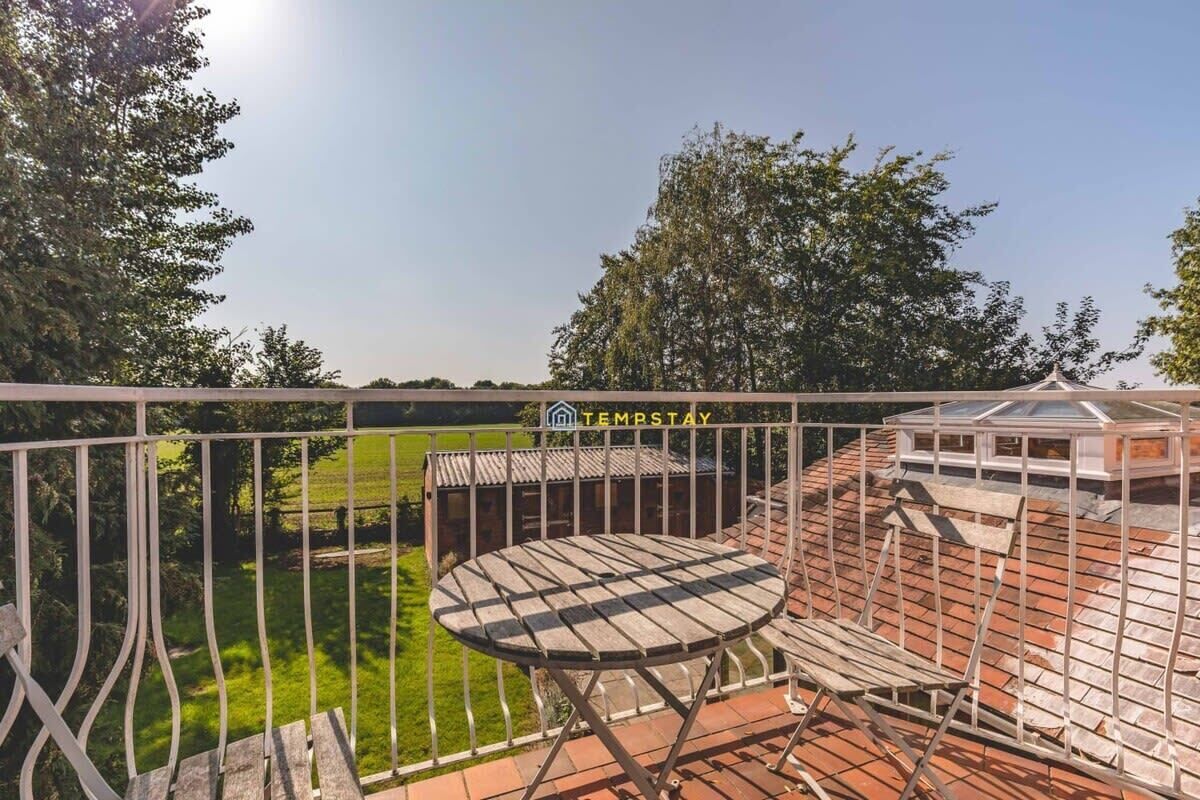 Un balcon avec une table et des chaises, une vue sur un paysage verdoyant et un bâtiment avec un toit en tuiles.