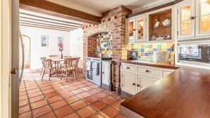 Una cocina con pared de ladrillo, armarios blancos, piso de baldosas y un comedor con sillas y una mesa.
