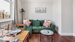 Un salon chaleureux avec un canapé vert, une petite table ronde et un coin repas comprenant une table et des chaises en bois.