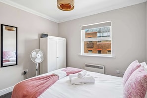 Ein Hotelzimmer mit einem Bett, einem weißen Schrank, einem Heizkörper, einem Fenster mit Blick auf ein Backsteinhaus und einem Deckenventilator.