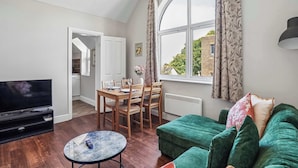 Un salon avec un téléviseur, une table à manger avec des chaises, un canapé vert et une fenêtre avec des rideaux.