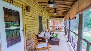 A wooden porch with a rocking chair, a sofa, and a table. - Log Cabin | Guadalupe River | Kayaks | Ping Pong (Seguin)