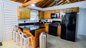 A compact kitchen with wooden cabinets, a black refrigerator, and a stainless steel trash can. - Log Cabin | Guadalupe River | Kayaks | Ping Pong (Seguin)