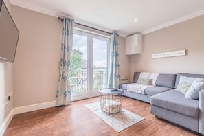 A living room with a grey sofa, a small round coffee table, and a large sliding glass door leading to an outdoor area.