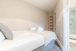 A bedroom with a bed, a bedside table, a towel, and a shower area.