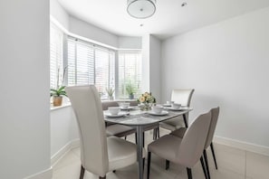 A dining area with a round table, six chairs, and a window with blinds. - 4-Bedroom Retreat in Slough - By Tempstay (Slough)