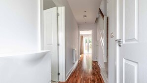 A hallway with white walls, wooden flooring, and white doors. - 4-Bedroom Retreat in Slough - By Tempstay (Slough)