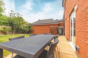 A patio area with a table and chairs, a brick wall, and a door. - 4-Bedroom Retreat in Slough - By Tempstay (Slough)