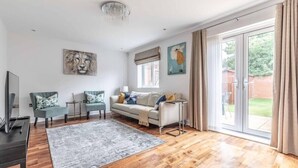 A modern living room with a sofa, two armchairs, a TV, and artwork on the walls. - 4-Bedroom Retreat in Slough - By Tempstay (Slough)