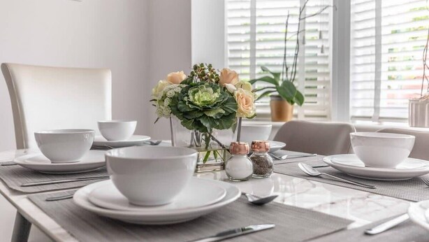 A dining table set with white plates, bowls, and cutlery, a vase with flowers, and salt and pepper shakers. - 4-Bedroom Retreat in Slough - By Tempstay (Slough)