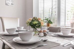 A dining table set with white plates, bowls, and cutlery, a vase with flowers, and salt and pepper shakers. - 4-Bedroom Retreat in Slough - By Tempstay (Slough)
