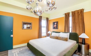 A hotel room with a green bed, two lamps, a disco ball chandelier, and a framed picture on the wall.