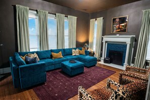 A living room with a sectional sofa, leopard print chairs, a fireplace, and large windows with curtains.