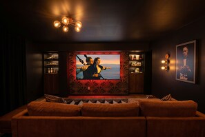 A dark-themed room with a large TV screen, a sofa, and shelves with bottles.
