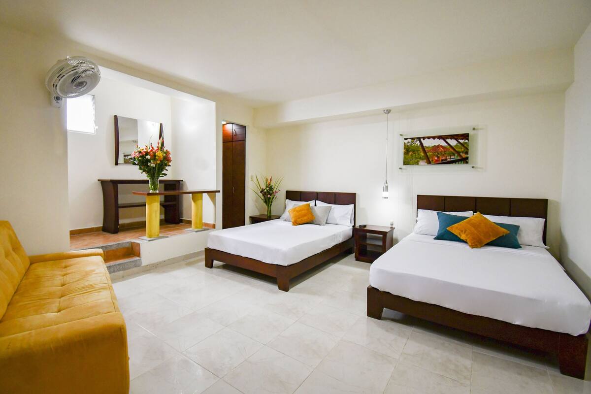 A hotel room with two beds, a sofa, a desk, and a mirror.