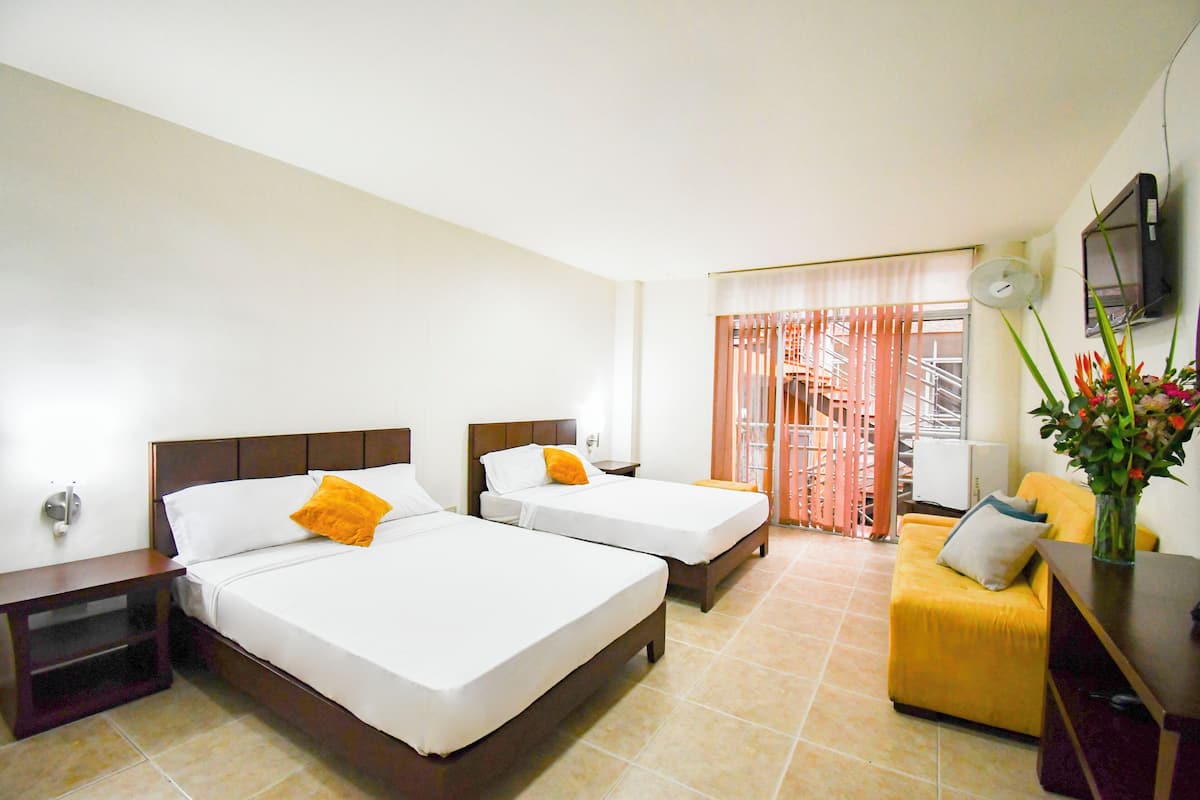 A hotel room with two beds, a sofa, a TV, and a window with curtains.