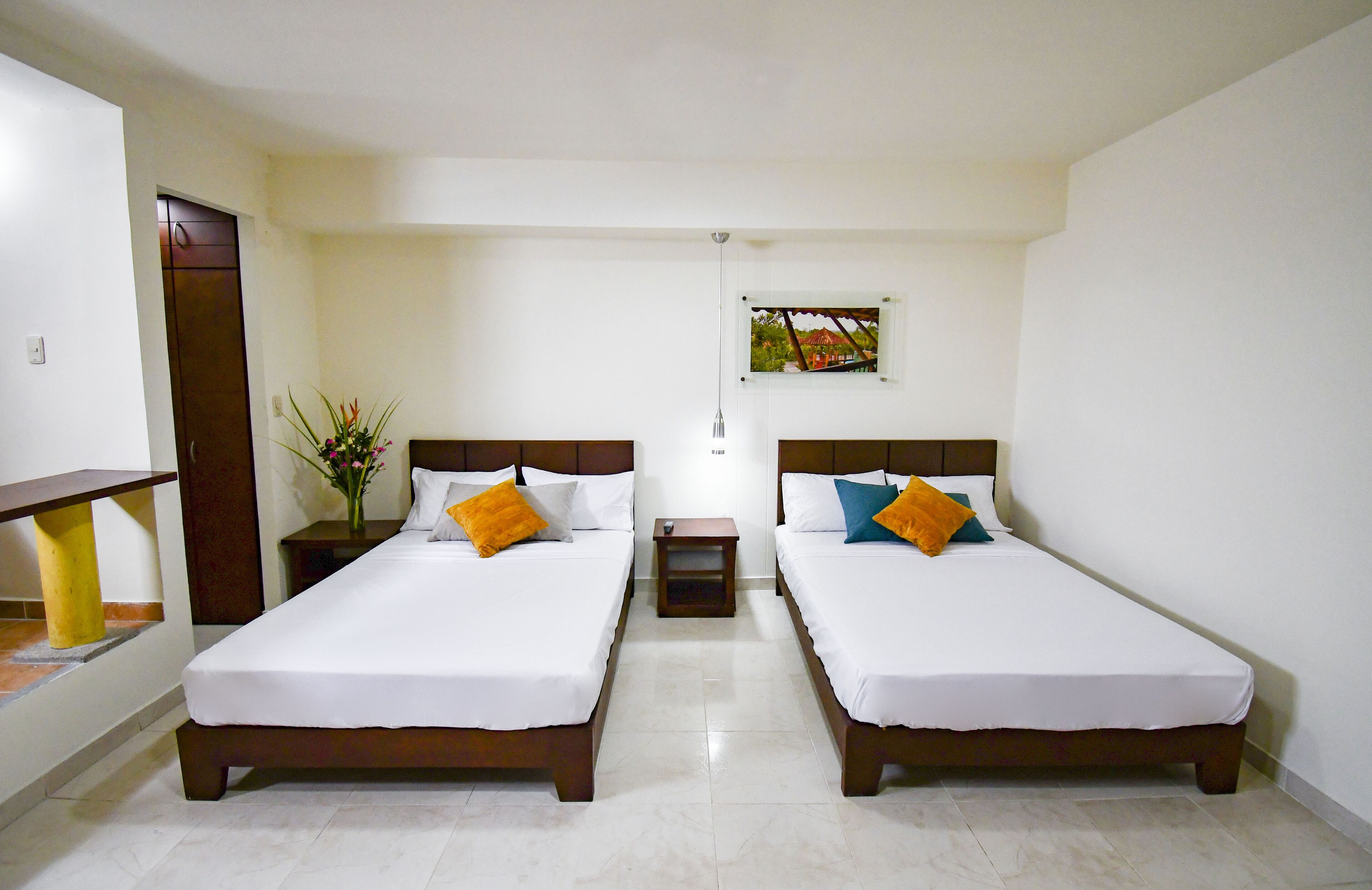 A hotel room with two single beds, a small nightstand, a potted plant, and a window with a view of trees.