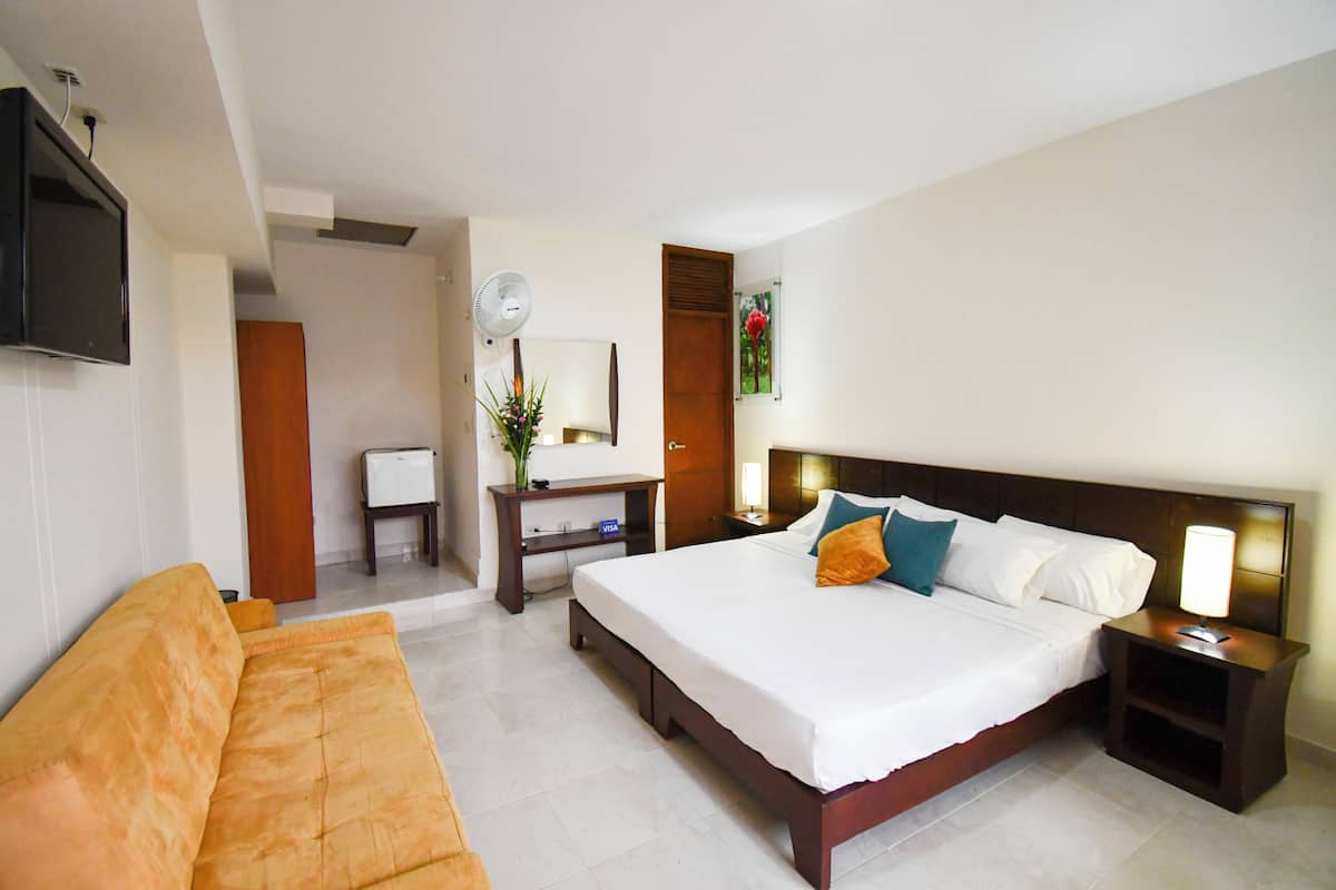 A hotel room with a large bed, a sofa, a desk with a computer, a TV, and a bedside lamp.