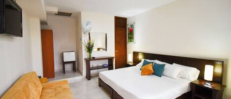 A hotel room with a bed, a sofa, a desk with a computer, a TV, and a bedside lamp.