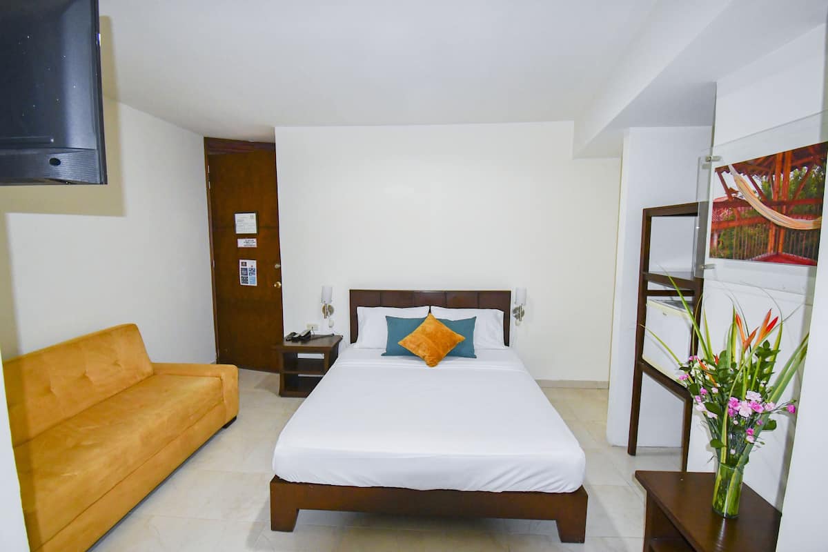 A bedroom with a bed, a sofa, a nightstand, a TV, and a wall-mounted shelf with a painting.