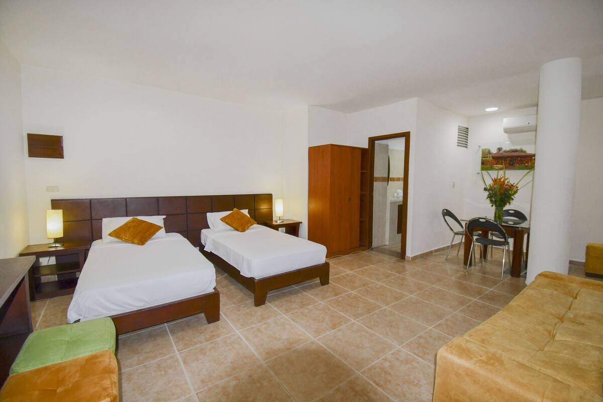 A hotel room with two beds, a desk, a chair, and a dining area.