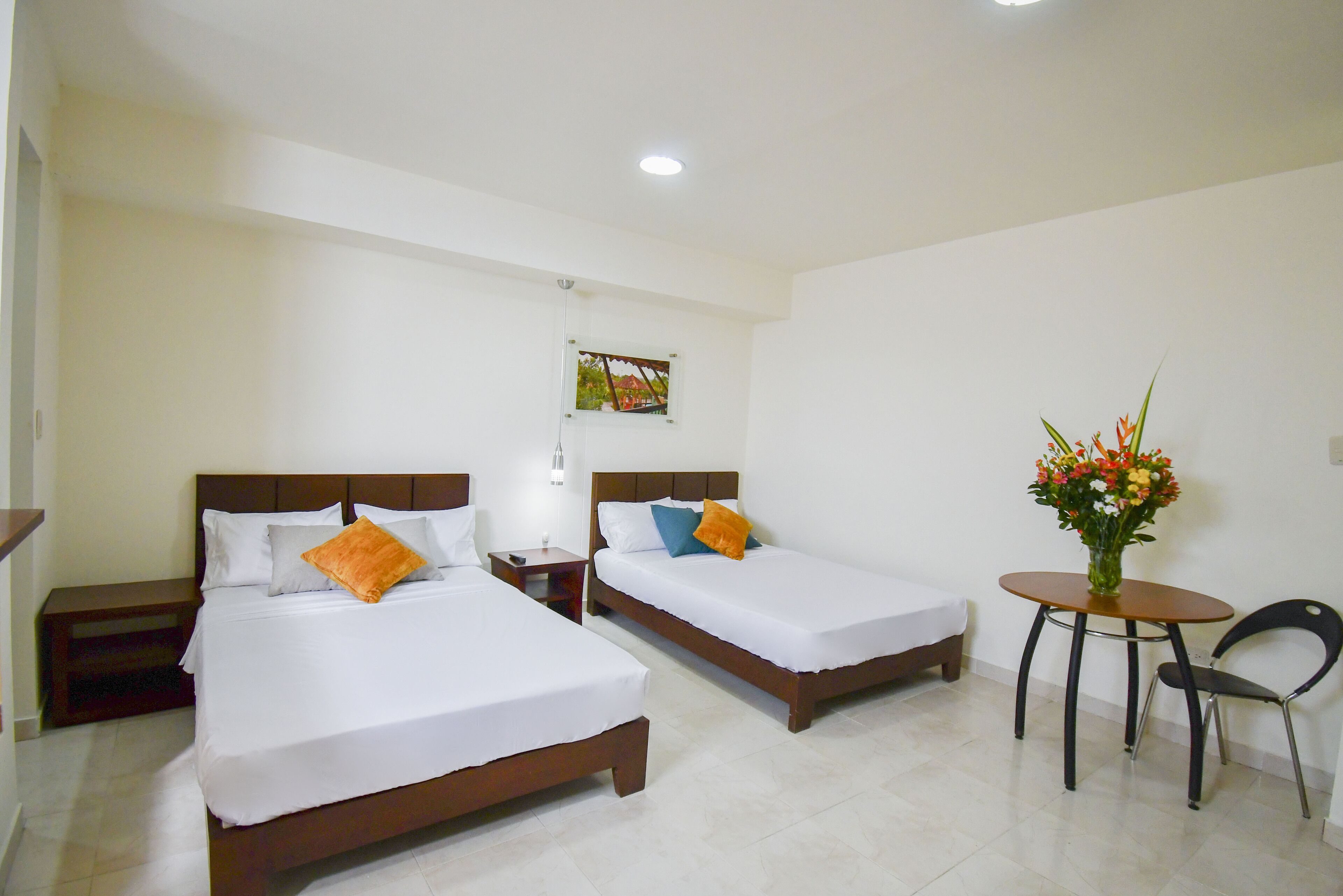 Une chambre d’hôtel avec deux lits simples, une petite table ornée d’un vase de fleurs, une chaise et une table de chevet avec une lampe.