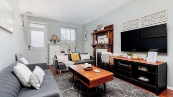 A modern living room with a grey sofa, a wooden coffee table, and a black entertainment unit with a flat-screen TV.