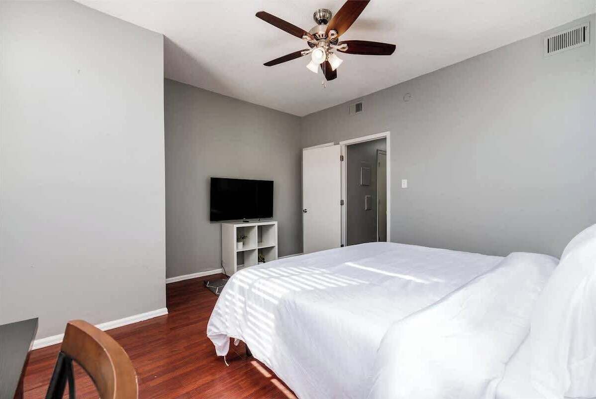 A bedroom with a bed, a ceiling fan, a TV, and a door.