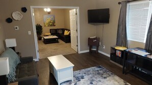 A living room with a sofa, coffee table, and a rug. There is a TV mounted on the wall and a window with curtains. - NEW!!! The Uptown Oasis...seconds from Uptown Marion!!!  (Marion)